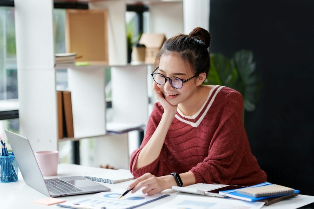 Beautiful Asian businesswoman working on her laptop enjoying work, taking note, reviewing work and r